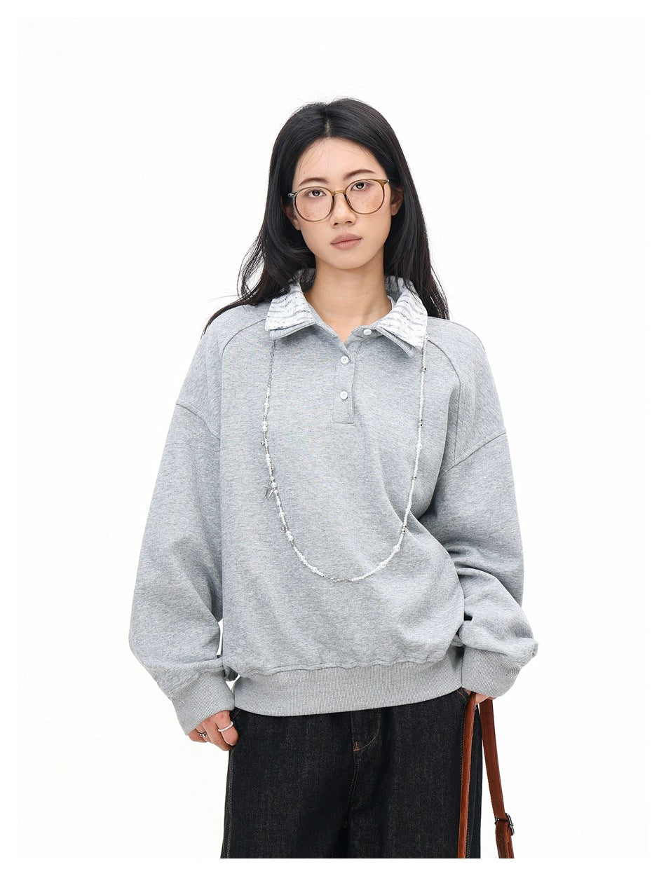 Model wearing a heather gray collared sweatshirt with striped collar, beaded necklace and dark jeans, front view