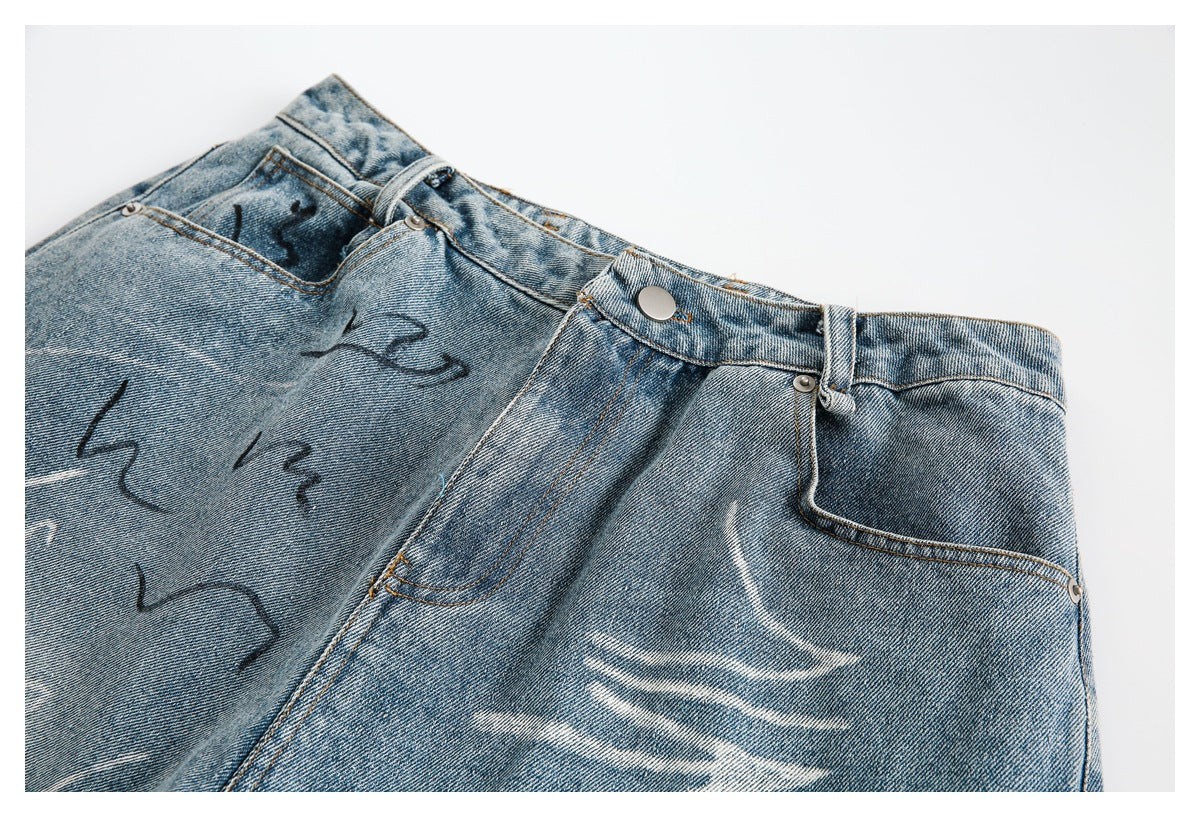 Close-up of the front waistband, button and pocket area of faded blue denim shorts with decorative markings.