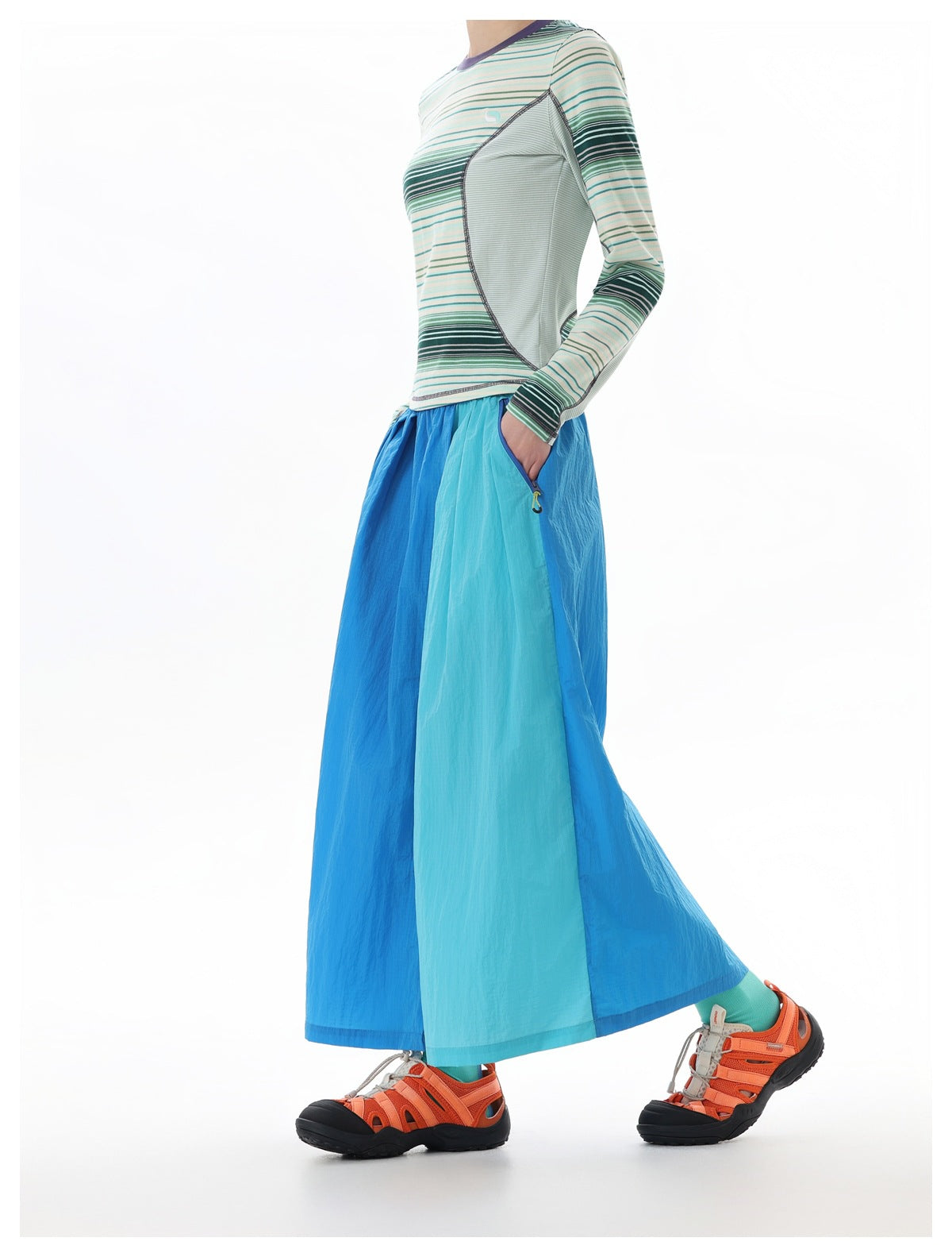 Side view of a model wearing a blue and aqua color-block maxi skirt with a striped long-sleeve top.