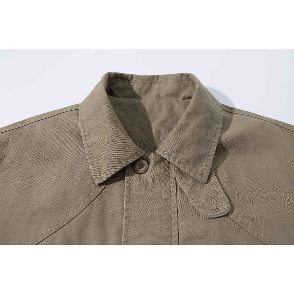 Close-up of a taupe jacket collar, button fastening, and small stitched motif on the collar tab.
