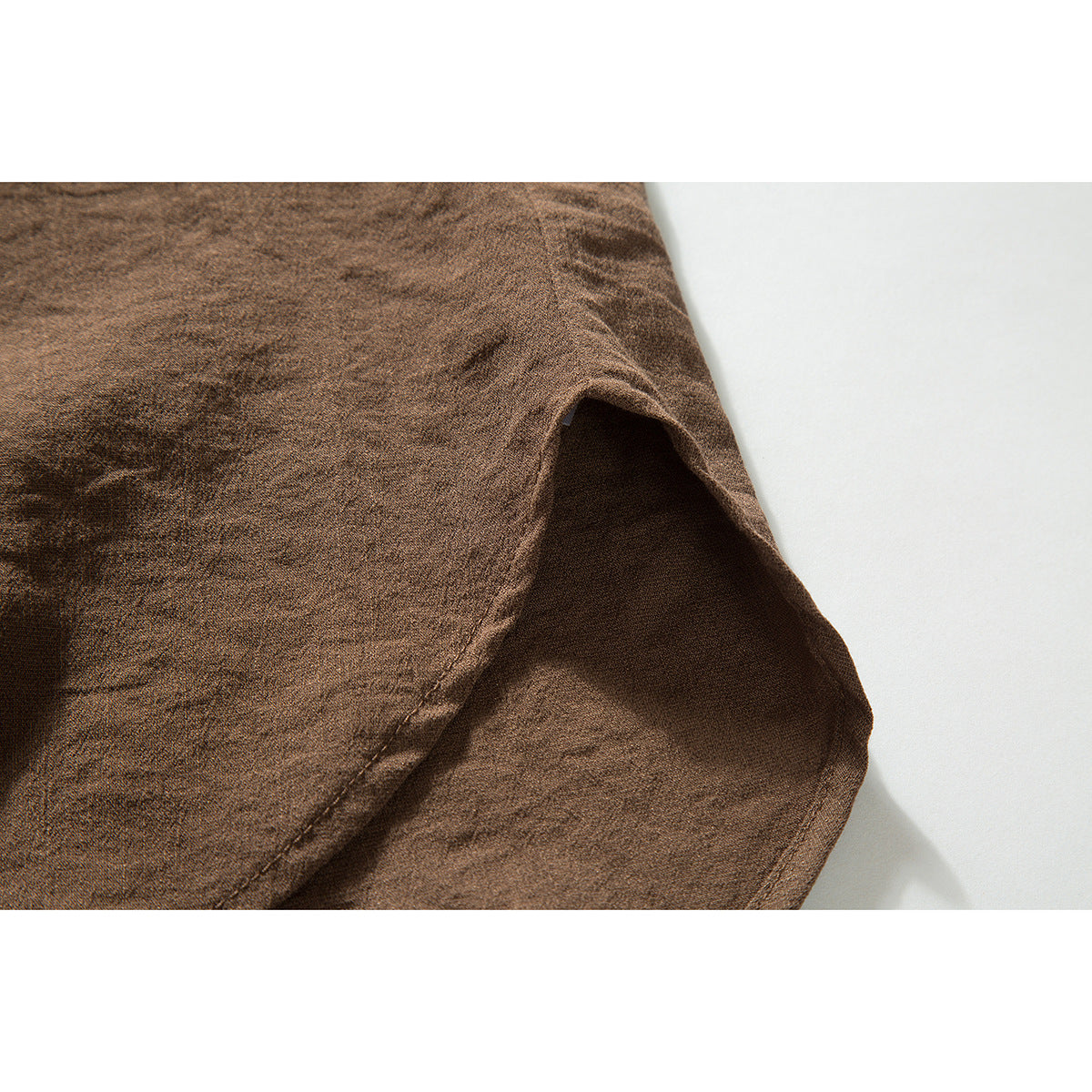Close-up of the brown shirt's curved sleeve opening and stitched seam.