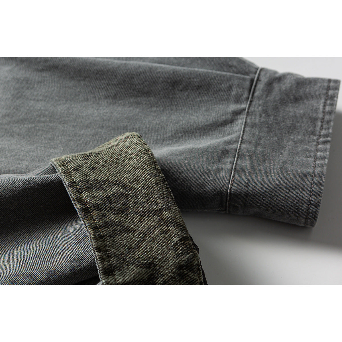 Close-up of a gray jacket sleeve with a wide cuff and mottled olive fabric visible underneath.