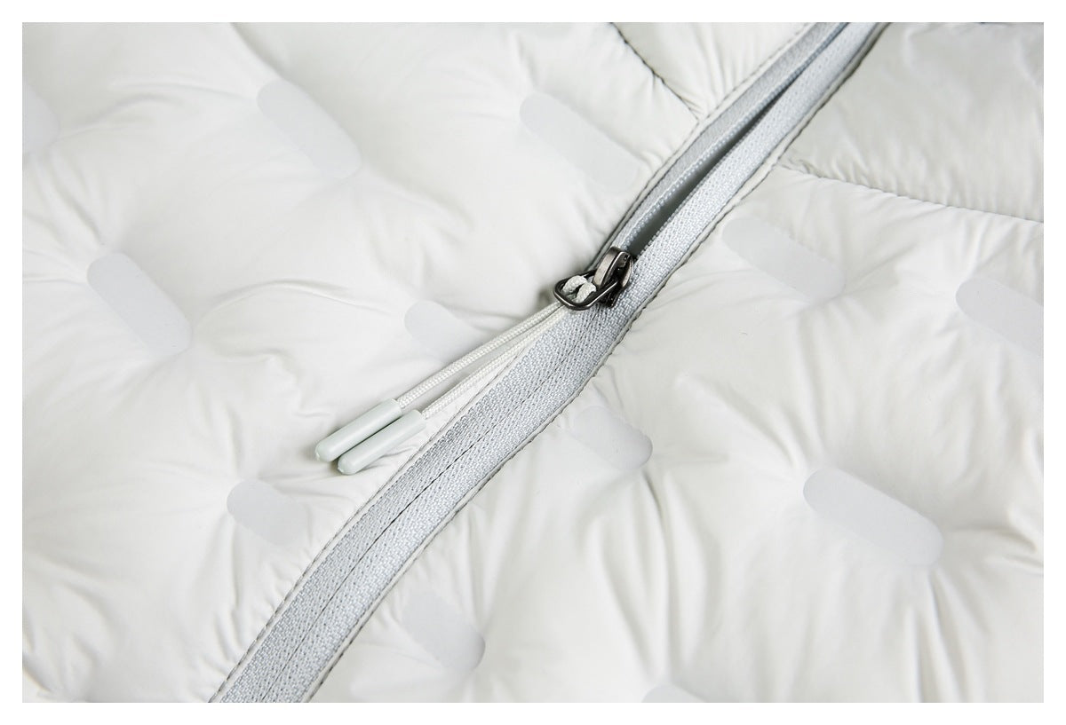 Close-up of the white padded jacket's gray zipper, metal slider, and paired pull cords against quilted panels.