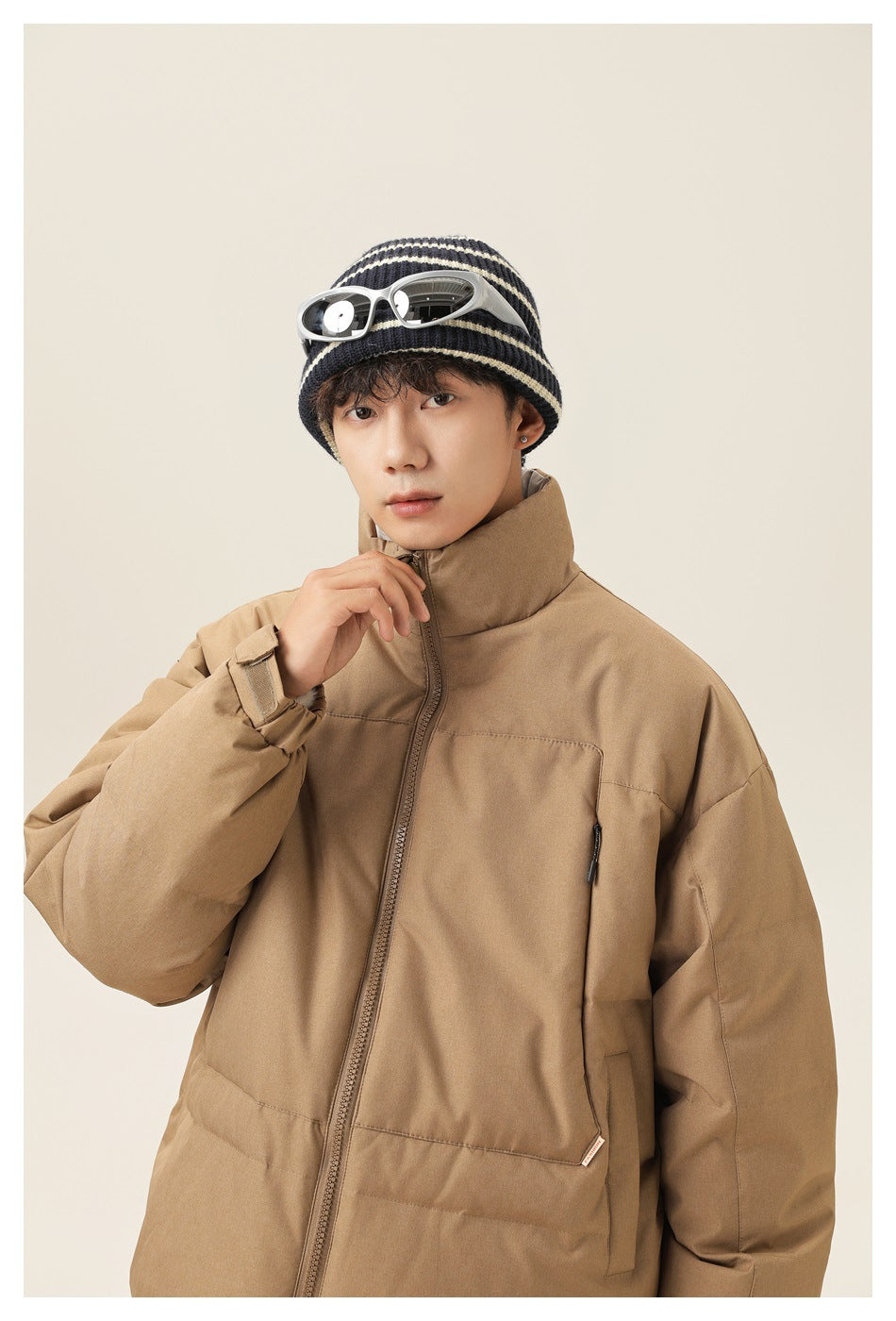 Close view of a model wearing a tan padded jacket with a high collar, front zip and zippered pockets.