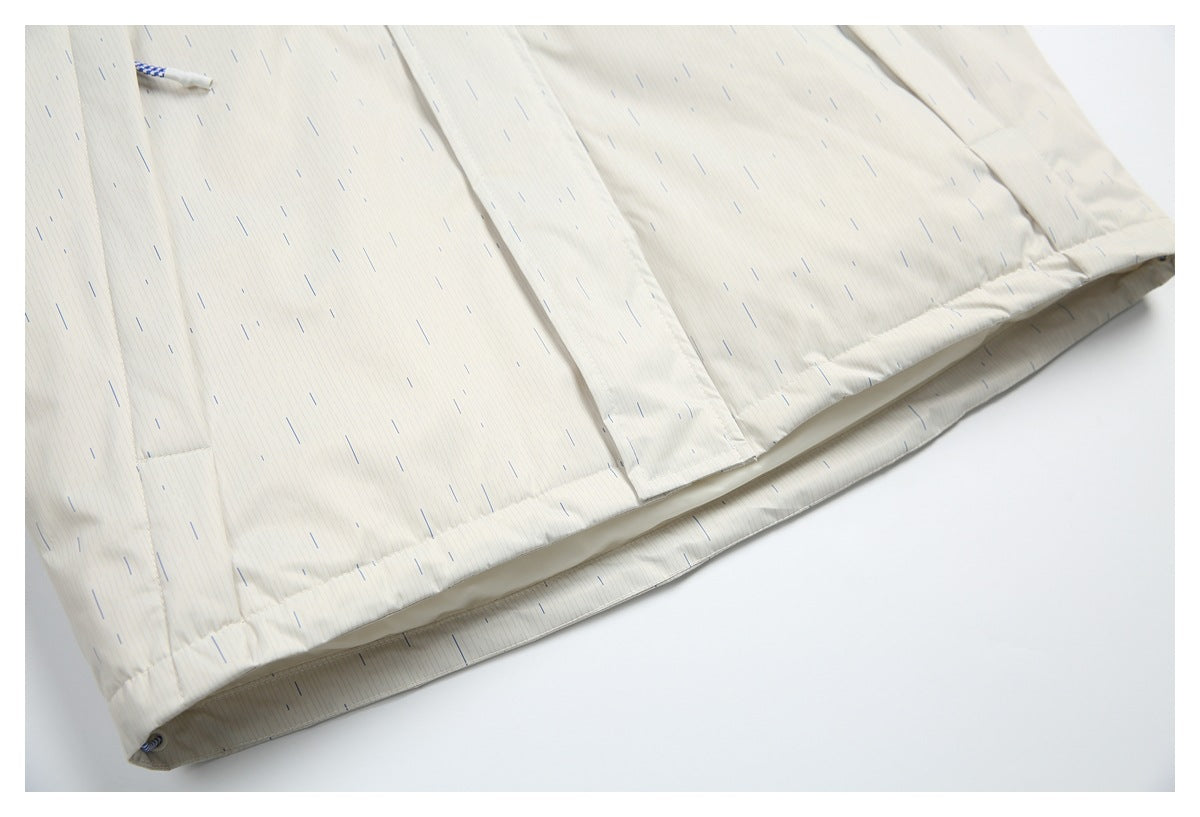 Close-up of the lower hem and seam on an off-white garment with fine blue-gray dashes; a cord end peeks out at the edge.