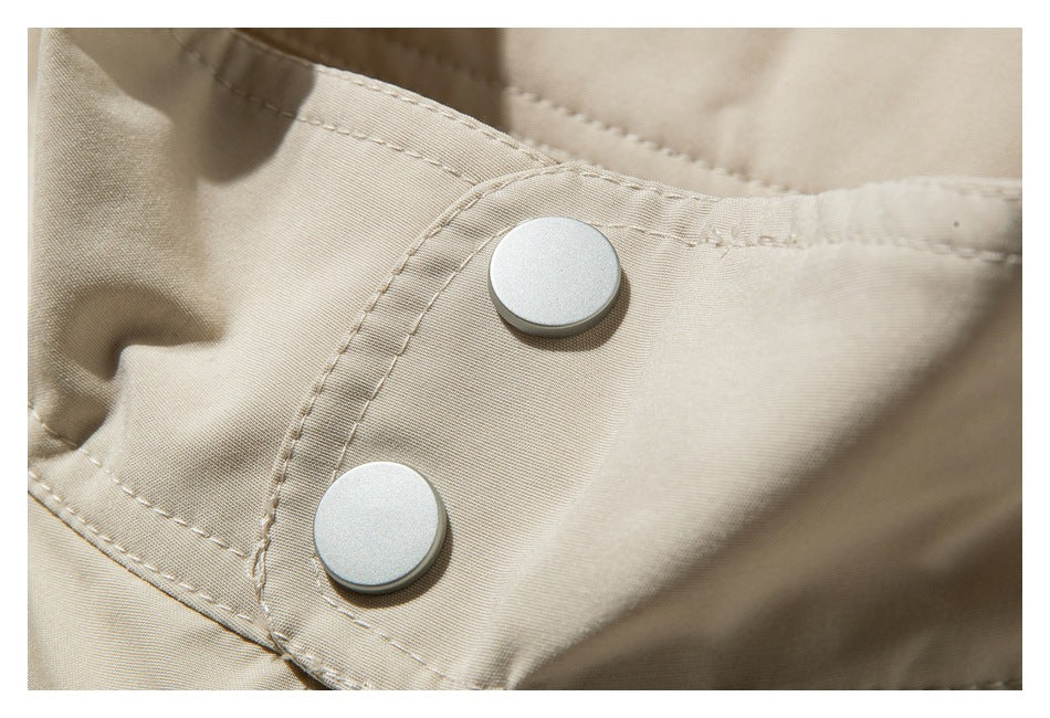 Close-up of two round silver snaps on a beige garment flap with visible stitching.