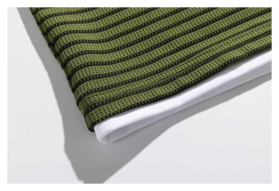 Close-up of the olive-green and black striped garment hem with a contrasting white layer underneath.