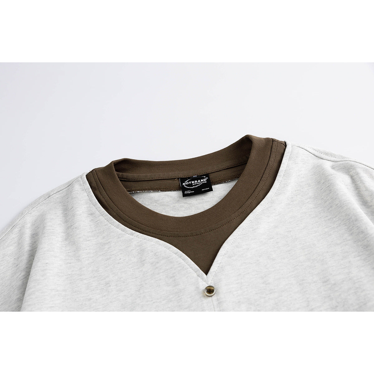 Close-up of a light gray shirt with a dark brown ribbed neckline, V-shaped front opening, and single button.