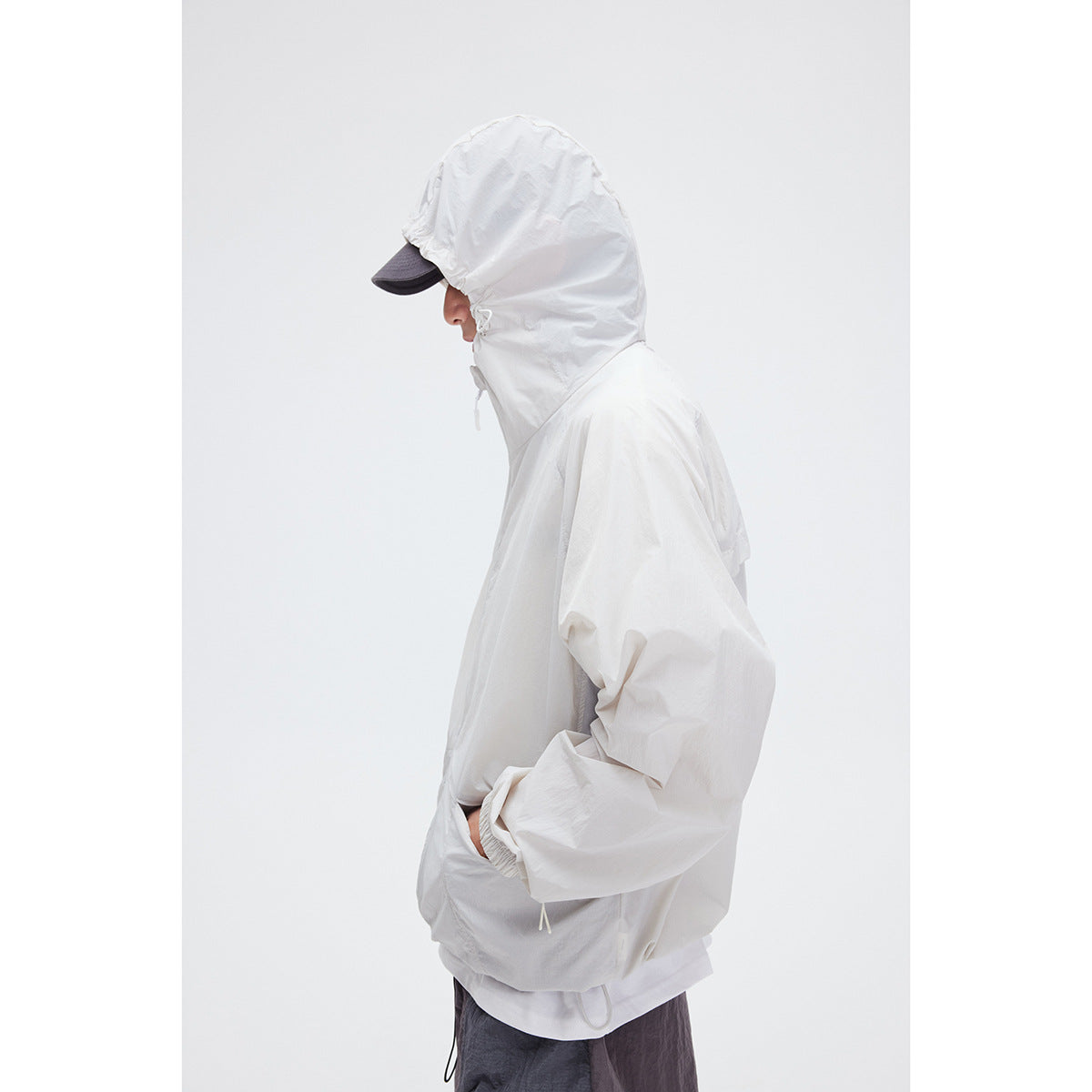 Side view of a model wearing a white hooded jacket with adjustable drawstrings and dark trousers.