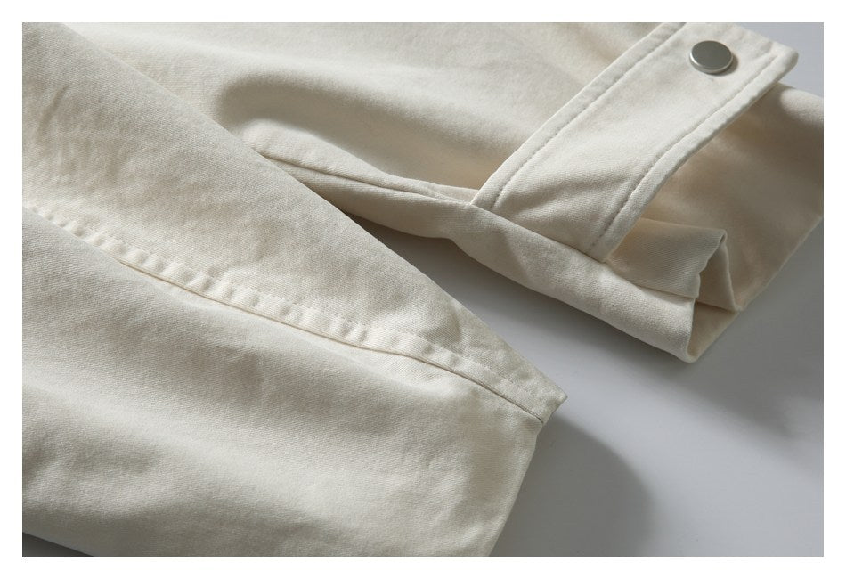 Close-up of ivory fabric with a stitched edge and a folded tab fastened by a metal snap.
