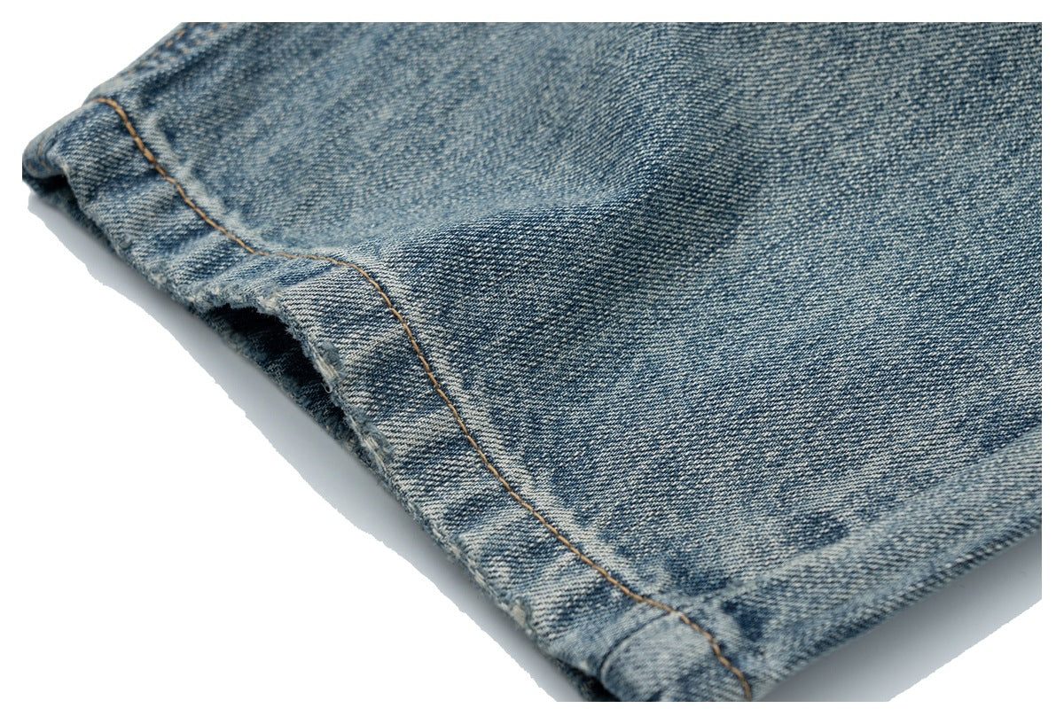 Close-up of the folded hem and tan stitching on faded blue denim jeans.