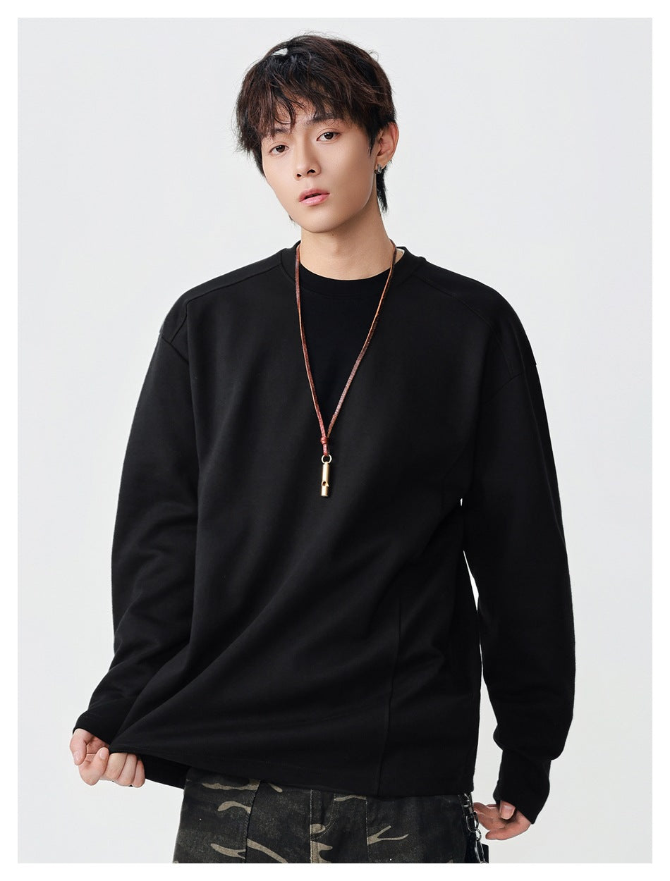 Model wearing a plain black long-sleeve crewneck top, holding the hem to show its loose fit.