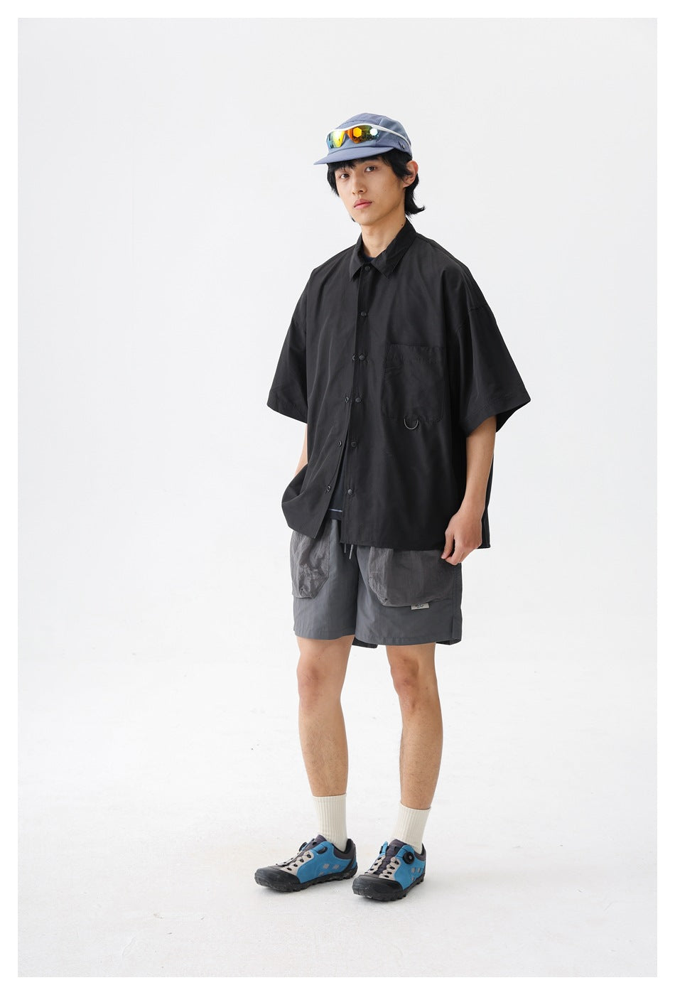 Full-length studio view of a model in an oversized black short-sleeve button-up shirt and gray shorts.