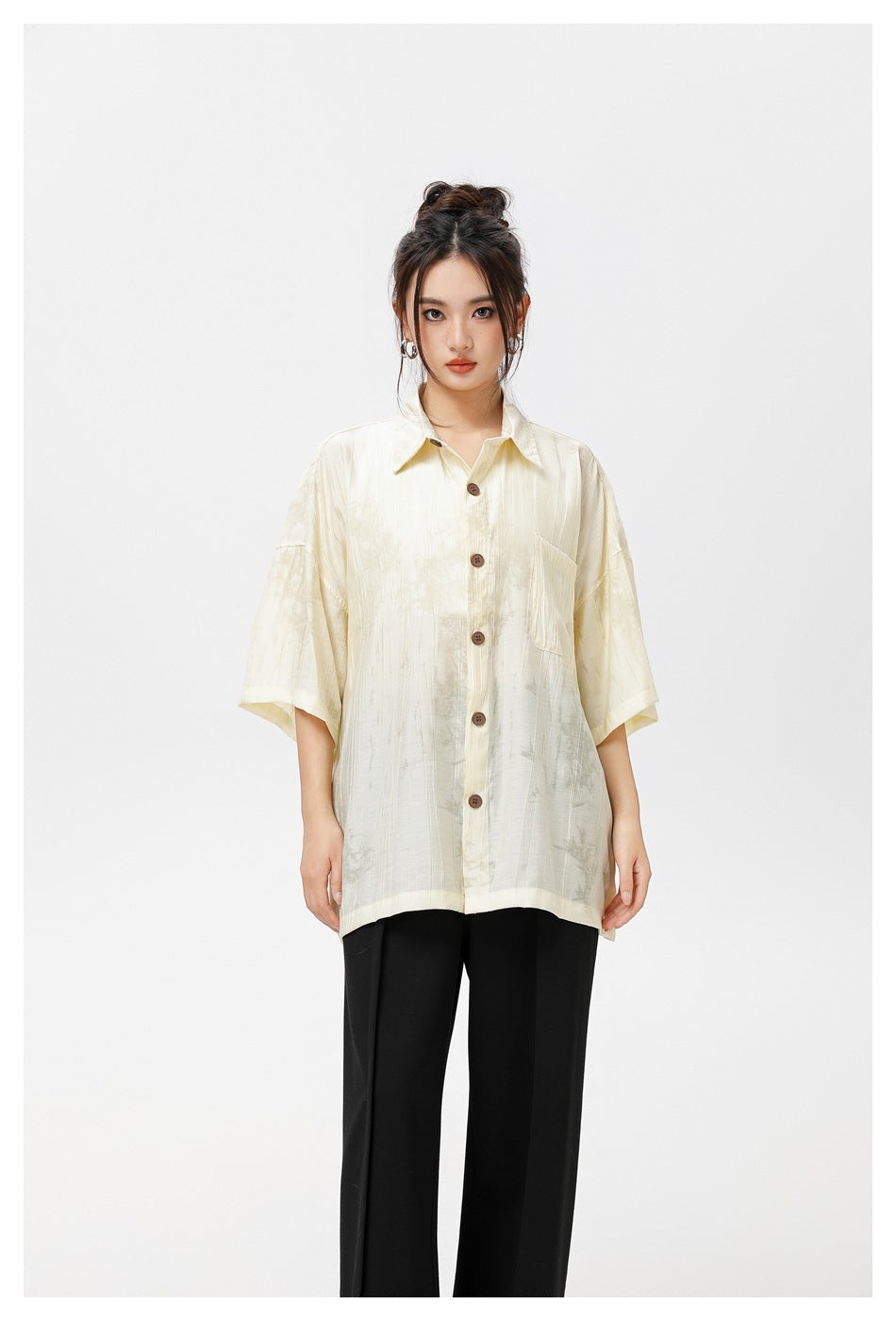 Close view of a model in a pale yellow short-sleeve button shirt with brown buttons, chest pocket and black trousers