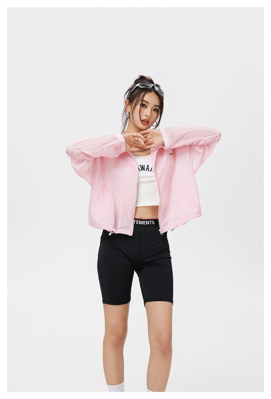 Model wearing an open light pink zip jacket with a stand collar and black cycling shorts.