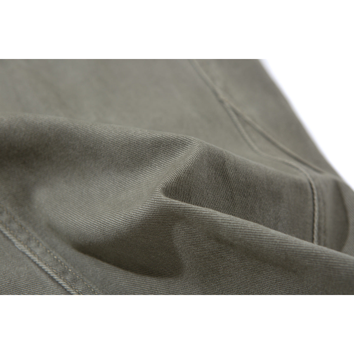 Macro view of olive-gray pants fabric, folded to show its surface texture and stitching.