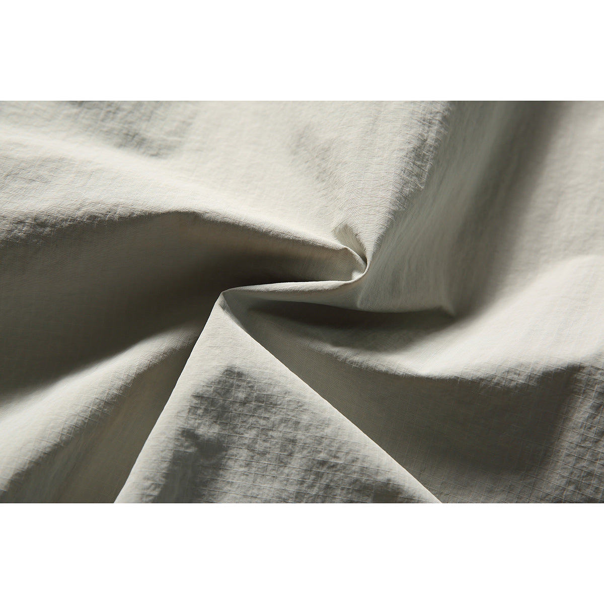 Close-up showing the lightly gridded texture and folds of light gray-beige jacket fabric.