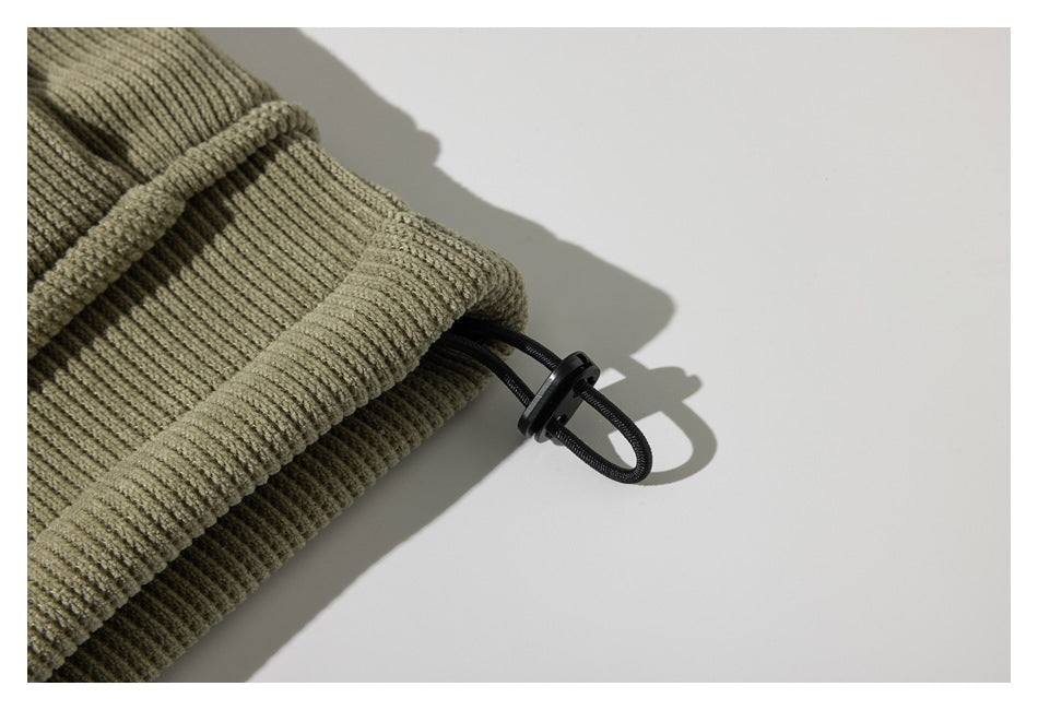 Close-up of an olive ribbed garment edge with a black elastic loop and toggle.