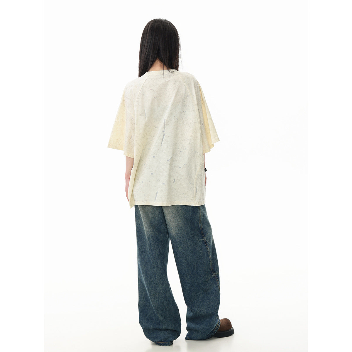 Back view of a model wearing an oversized ivory, gray-speckled T-shirt with loose dark blue jeans.