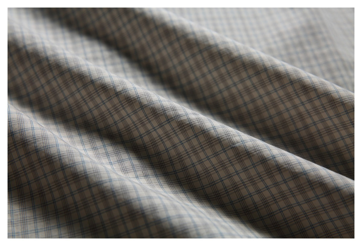 Close-up of draped beige fabric with a fine blue-gray plaid pattern.