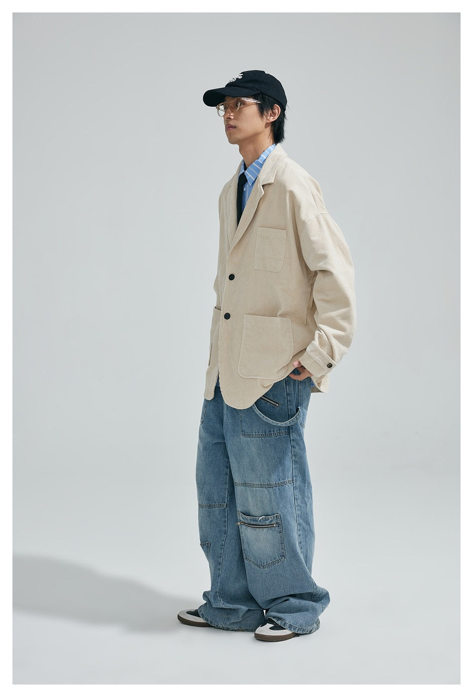 Side view of a model wearing an oversized cream corduroy blazer with patch pockets and loose blue jeans.