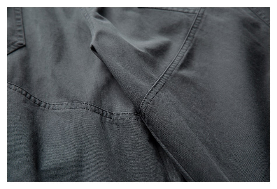 Close-up of dark charcoal pants showing intersecting stitched seams and a folded fabric panel.