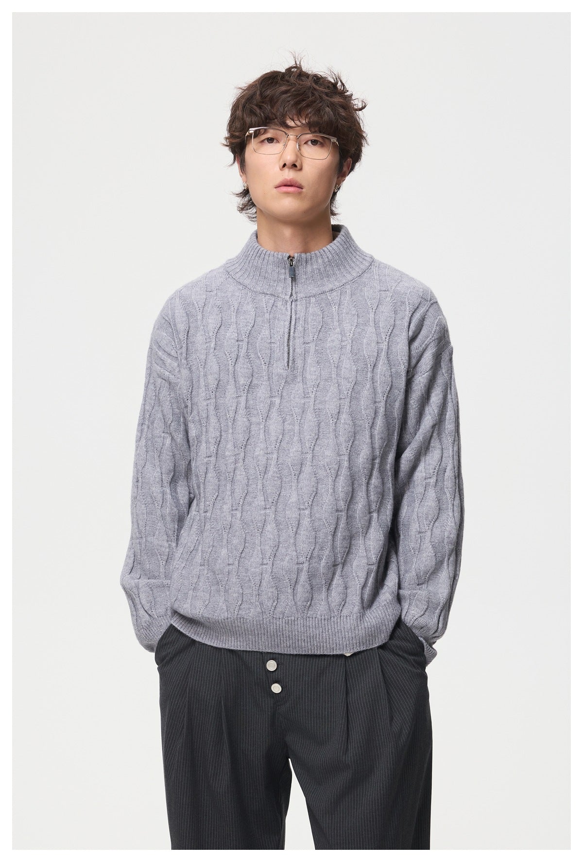 Model wearing a light gray cable-knit sweater with a ribbed stand collar and short zip over dark pinstripe trousers.