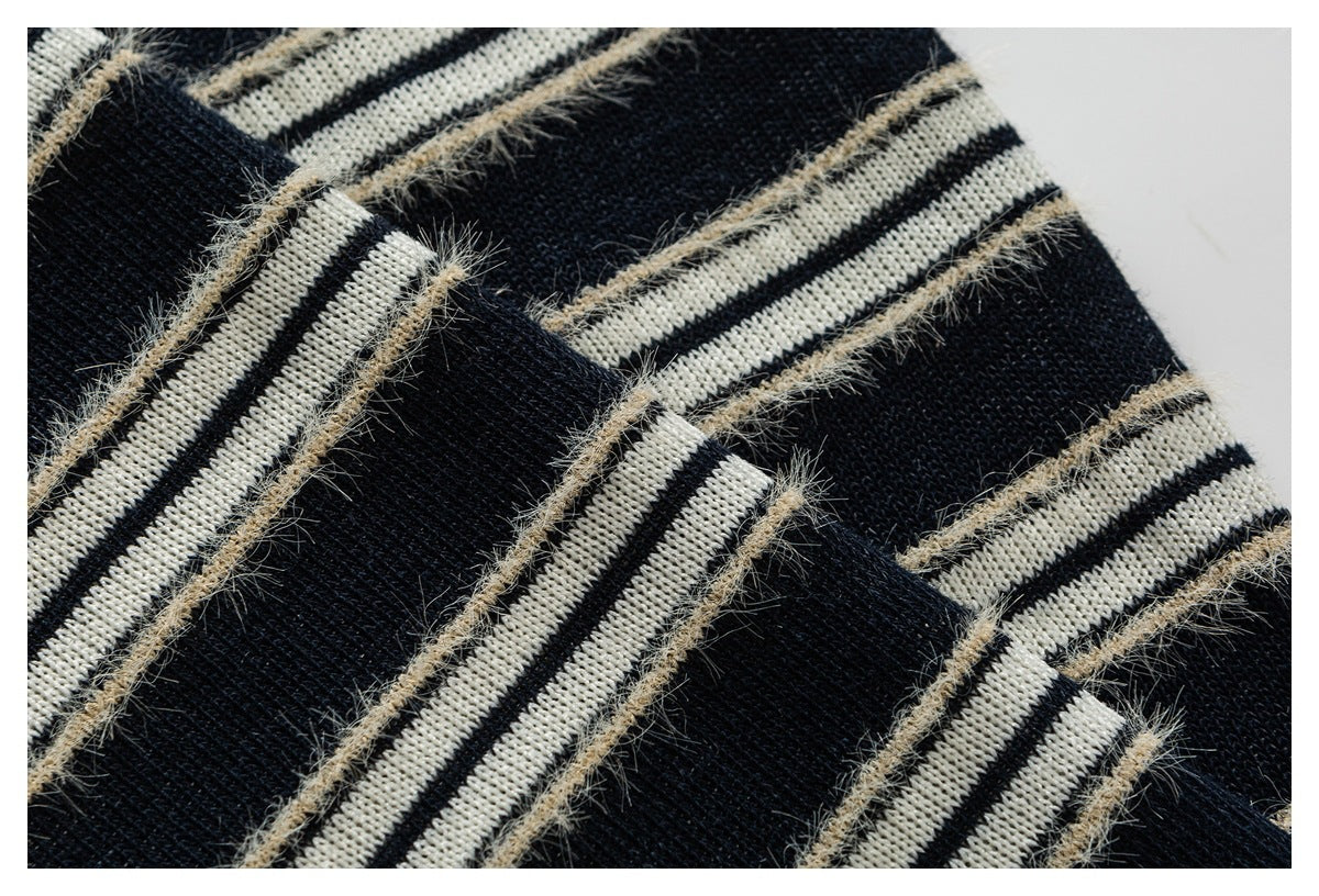 Close-up of black knit fabric with cream striped bands and fuzzy tan yarn detailing.