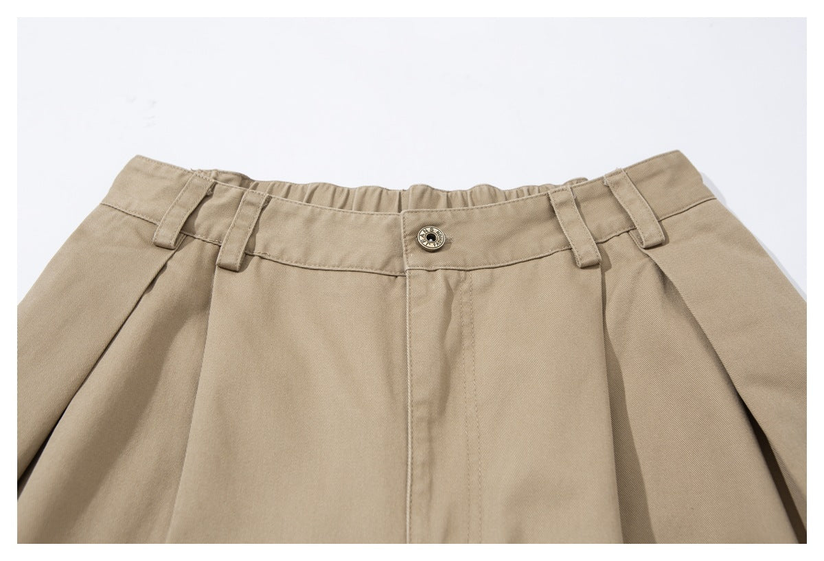 Close-up of tan shorts showing the waistband, belt loops, pleats and a metal button.