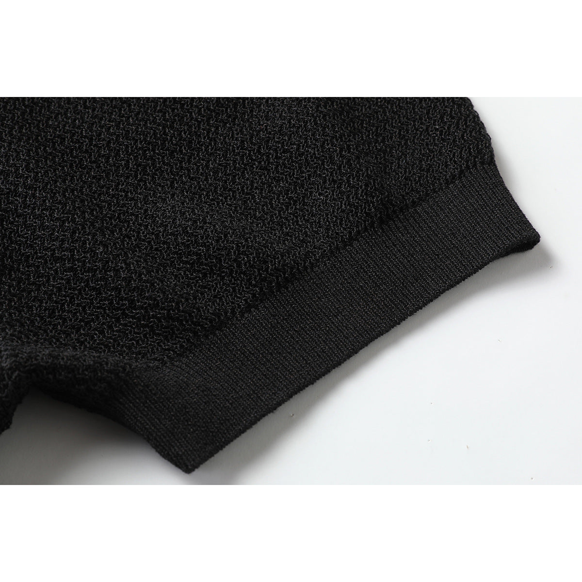 Close-up of the black polo shirt's textured knit and ribbed sleeve cuff.