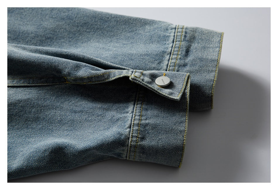 Close-up of a blue denim jacket cuff and metal button with yellow stitching.
