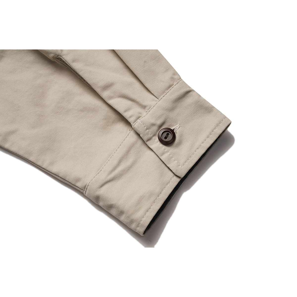 Close-up of a beige shirt cuff with a dark button, stitching, and a narrow dark inner edge.