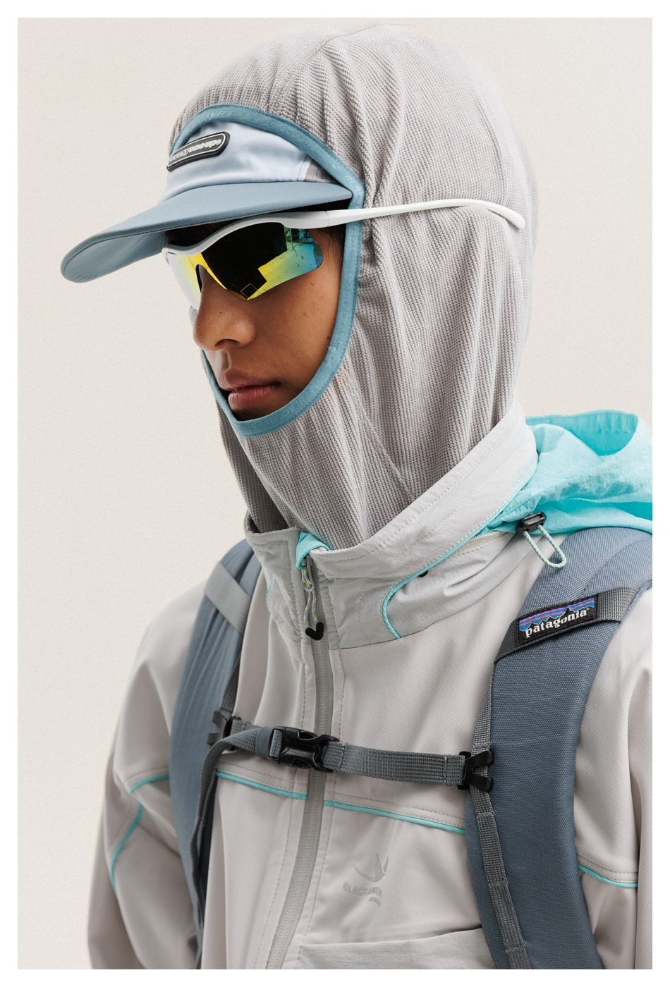 Close-up of a model's gray hood and cap, mirrored sunglasses, and the turquoise-trimmed collar and chest of a jacket.