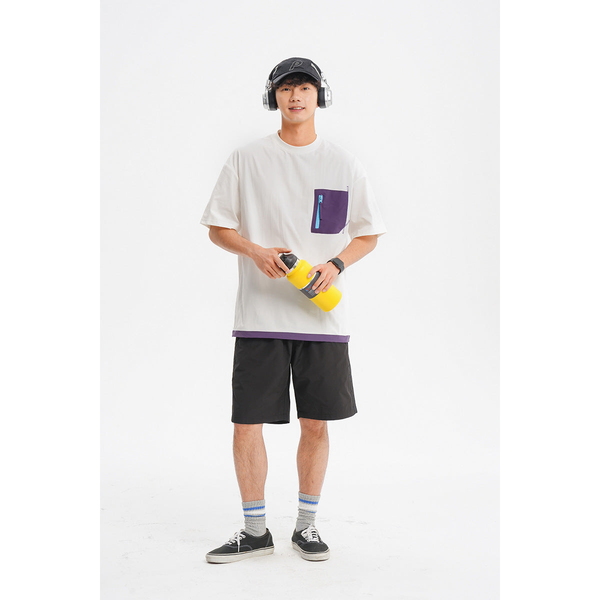 Model wearing a white oversized T-shirt with a purple zip chest pocket, black shorts, and a black cap.