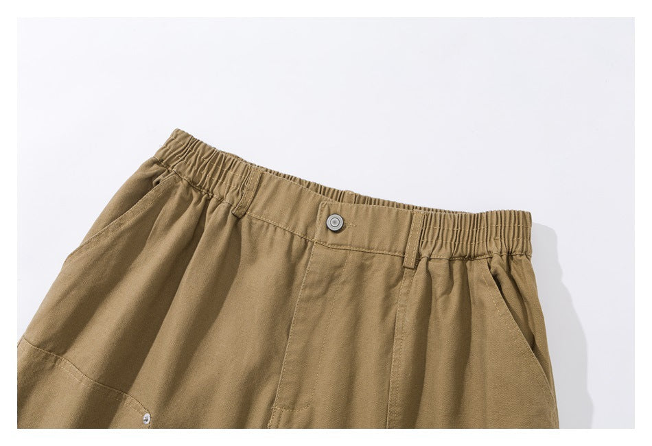 Close-up of tan shorts showing the elastic waistband, button closure, belt loops, and front pocket.