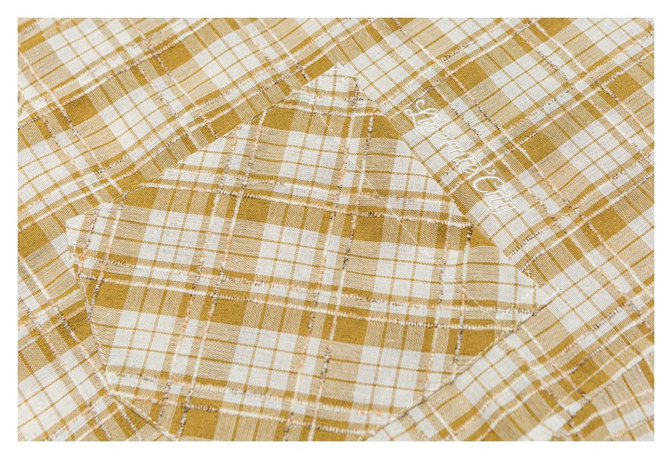 Close-up of a rounded patch pocket and white script embroidery on a mustard-and-white plaid shirt.
