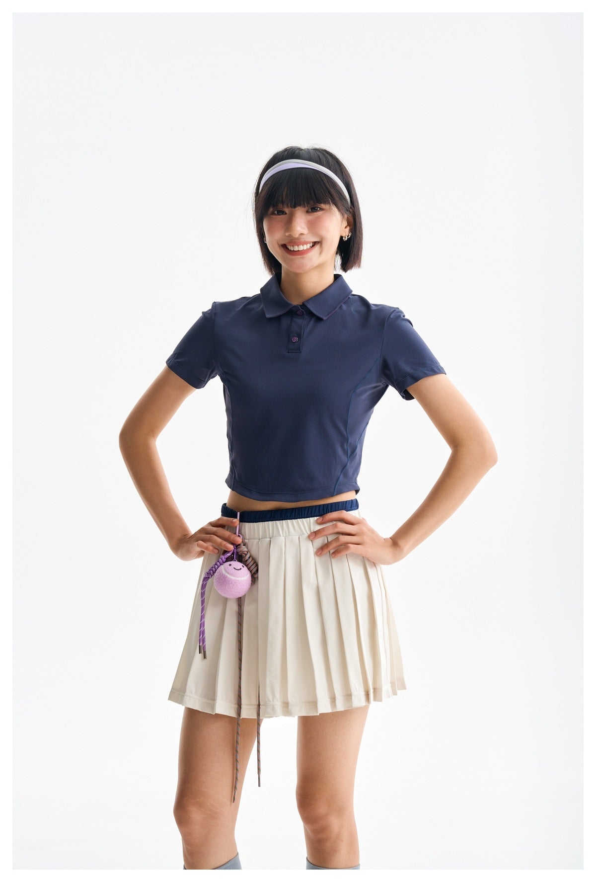 Model wearing a navy cropped polo and ivory pleated skirt, shown from head to mid-thigh.