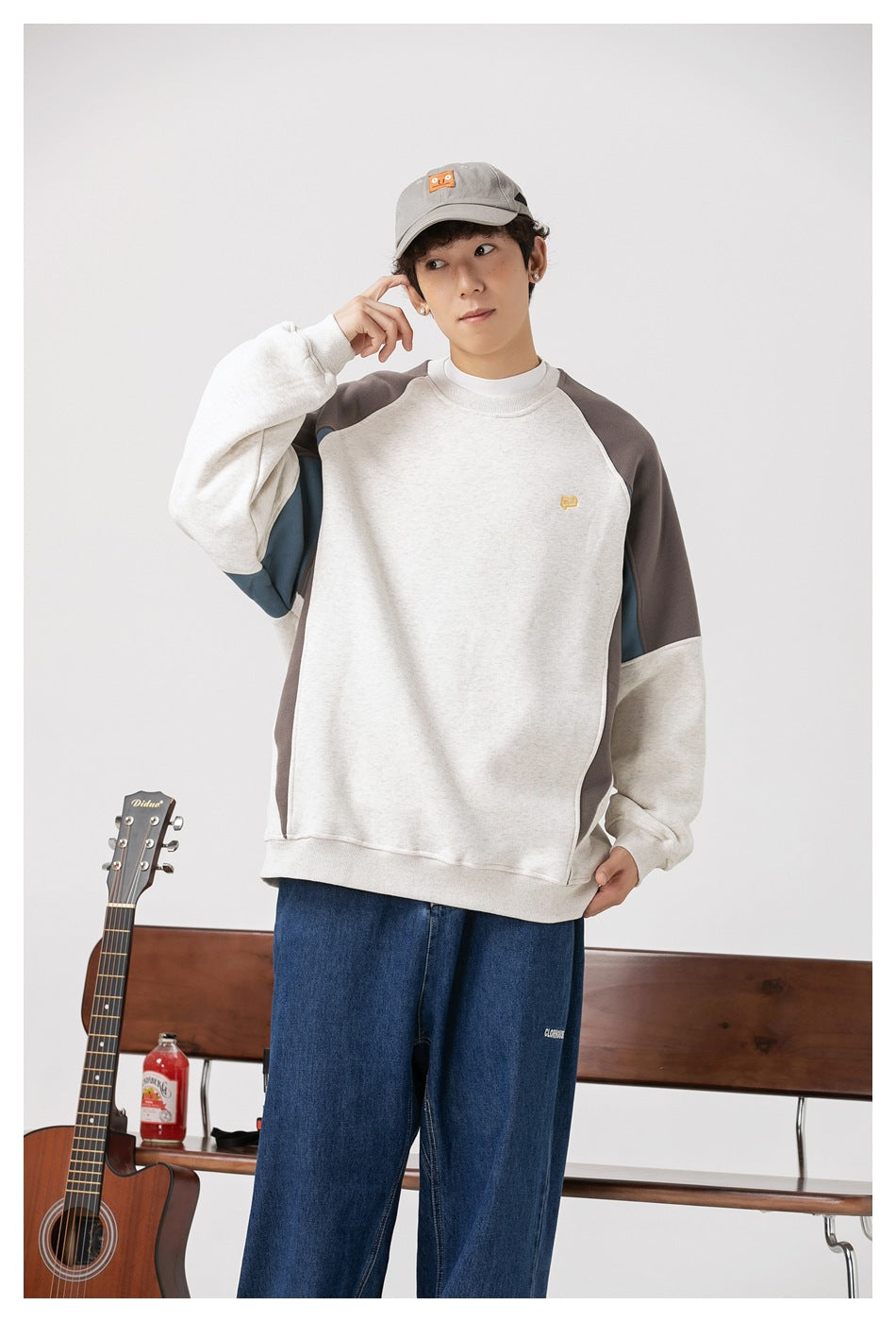 Model wearing a color-block raglan crewneck sweatshirt with an oatmeal body, charcoal shoulders, and blue side panels.