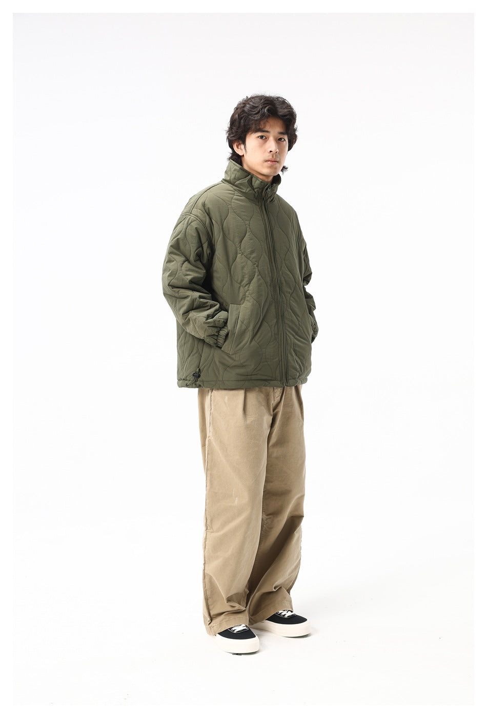 Model wearing army green quilted jacket with hands in pockets and khaki pants, angled view