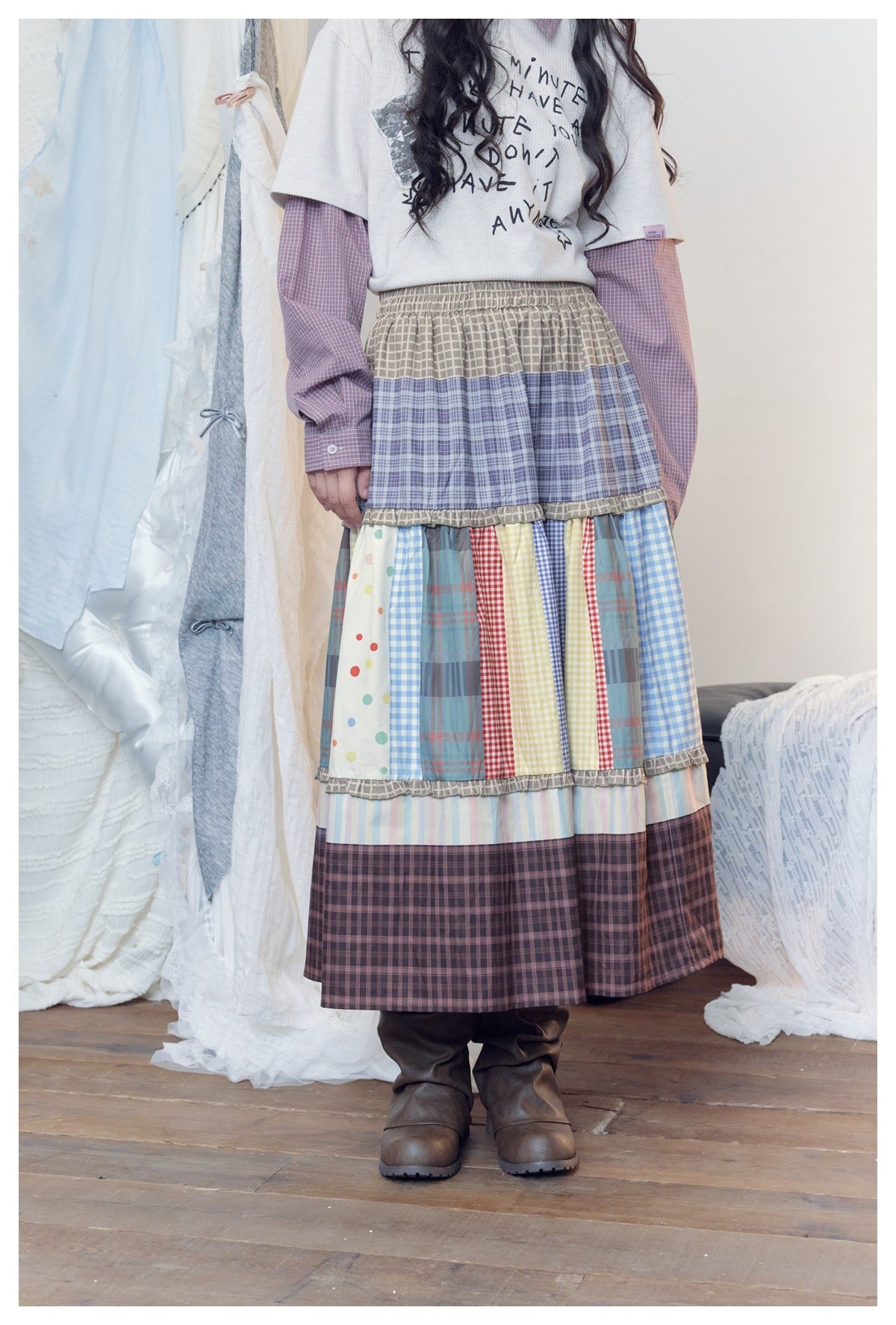 Person wearing the multicolor tiered patchwork long skirt with a graphic tee, plaid sleeves and brown boots