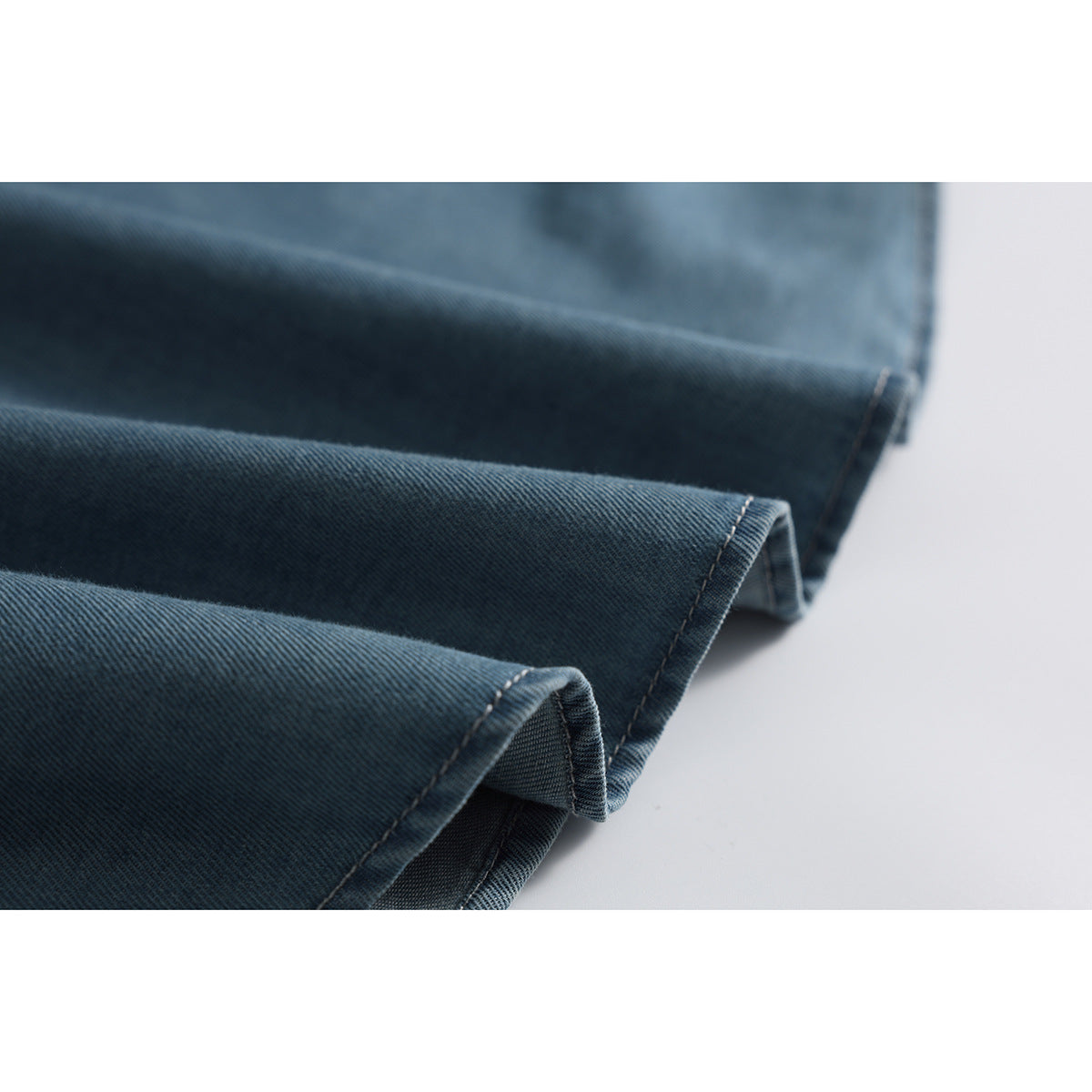 Close-up of the folded, stitched hem of a blue denim shirt.