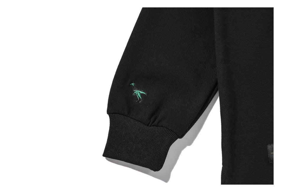 Close-up of a ribbed cuff and small green embroidered motif on the sleeve of a black shirt.