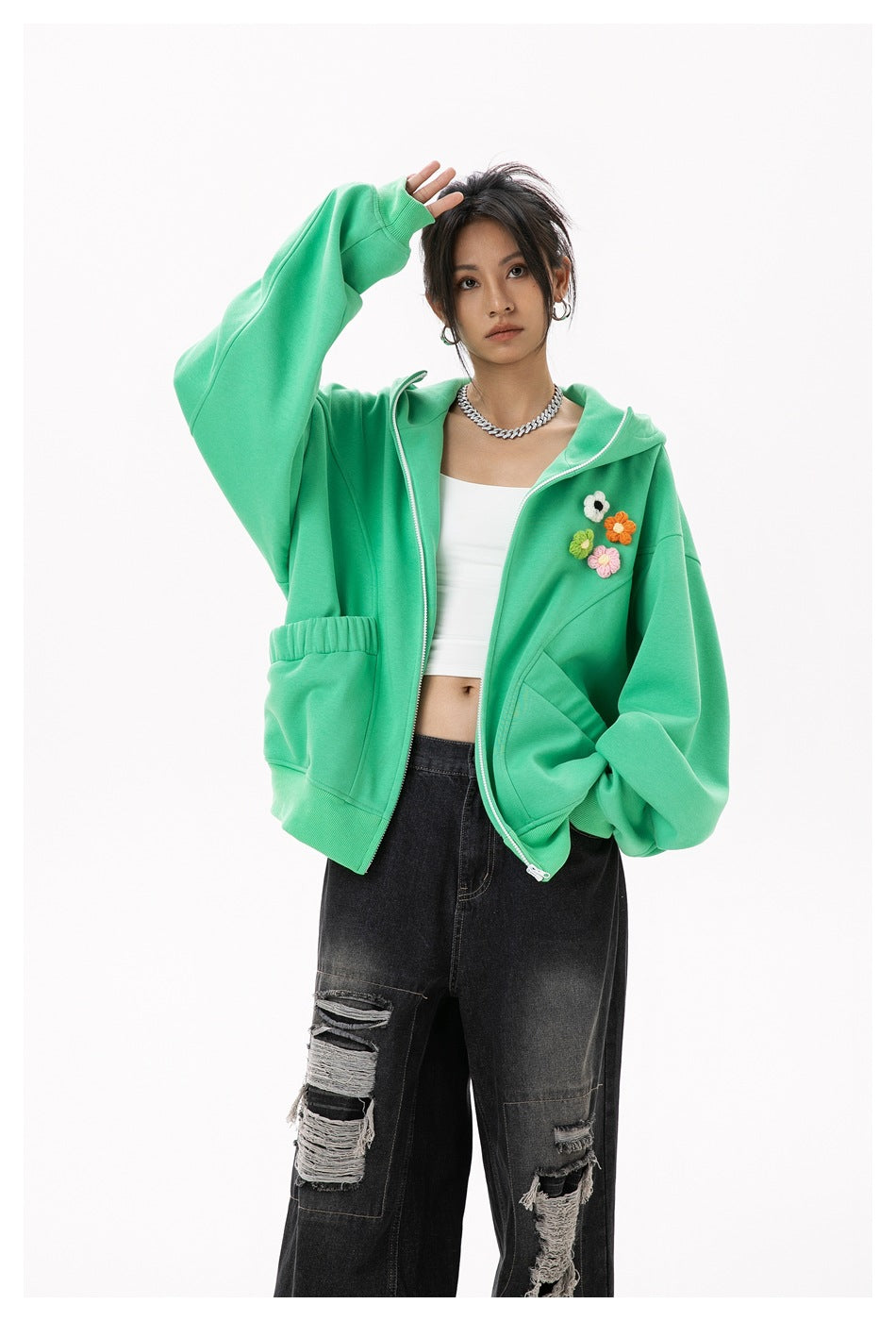 Model wearing an open mint-green hoodie with colorful flower appliqués and distressed black jeans.