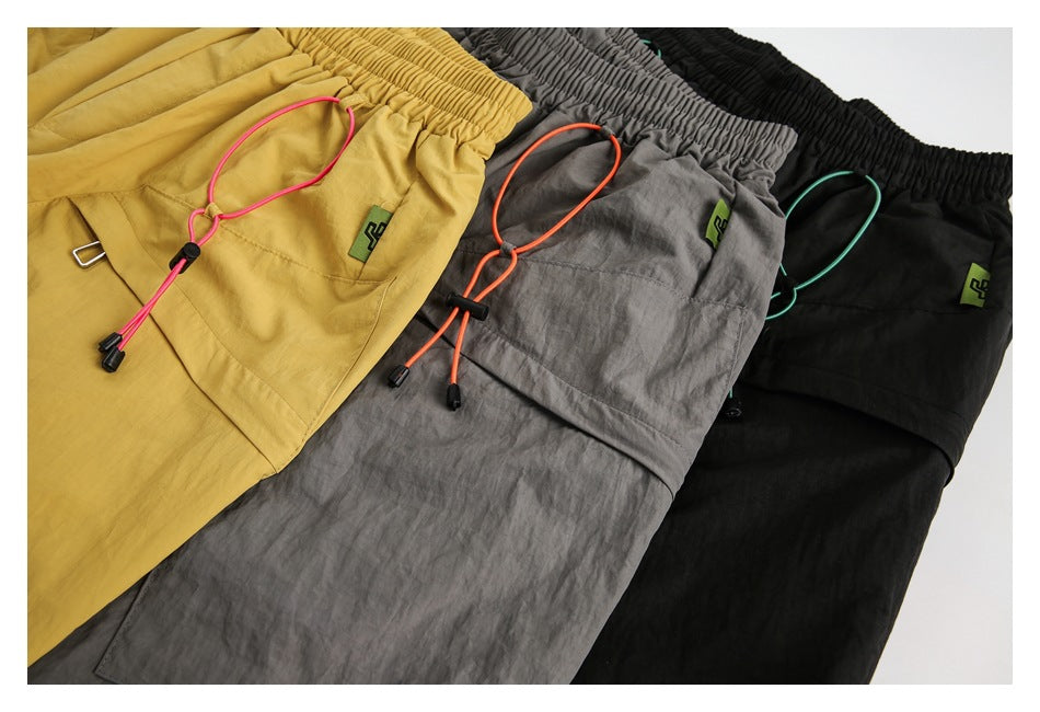 Mustard, gray, and black shorts laid together, showing front pockets, elastic waists, and adjustable drawcords.