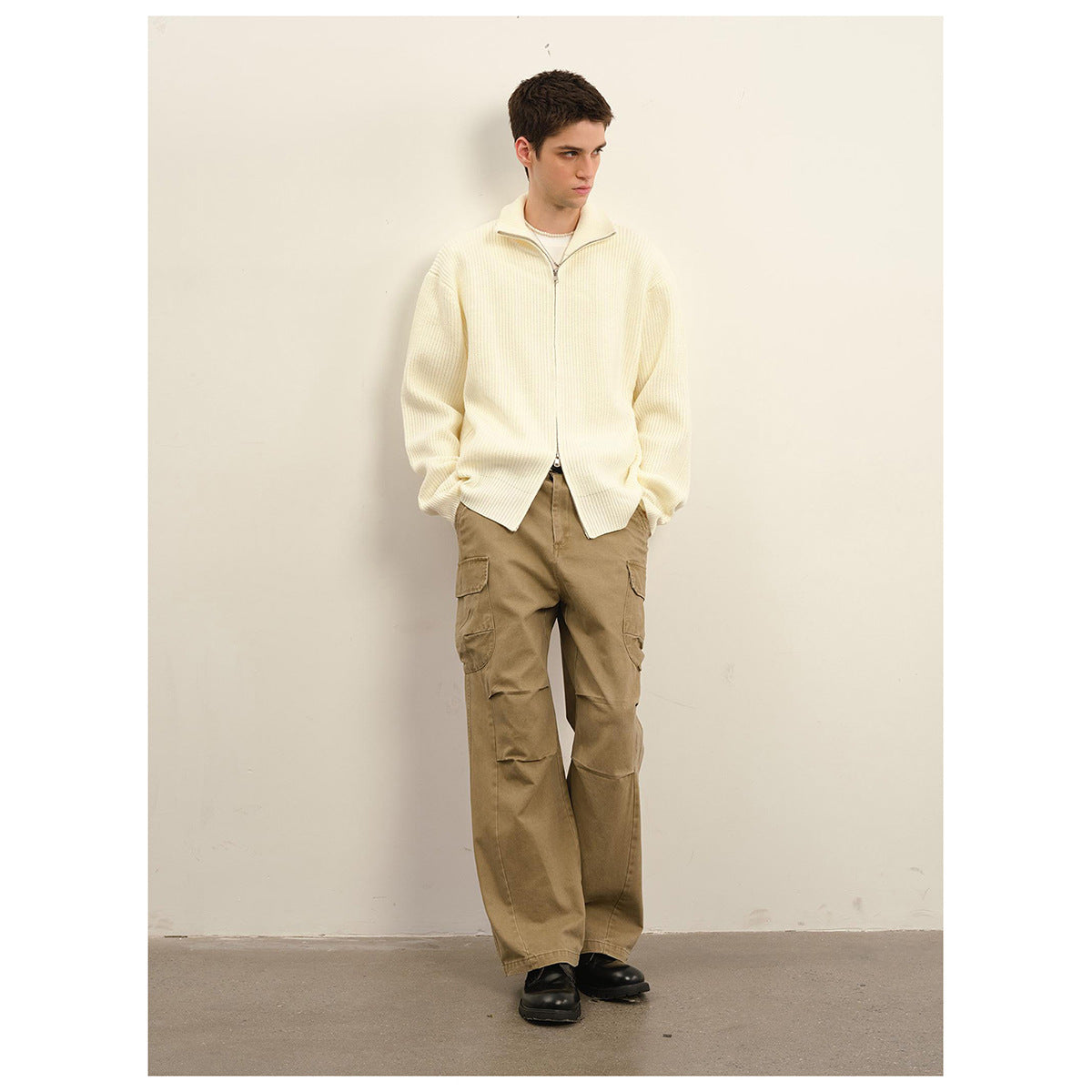 Model wearing an ivory ribbed zip-front sweater with a high collar and tan cargo trousers.