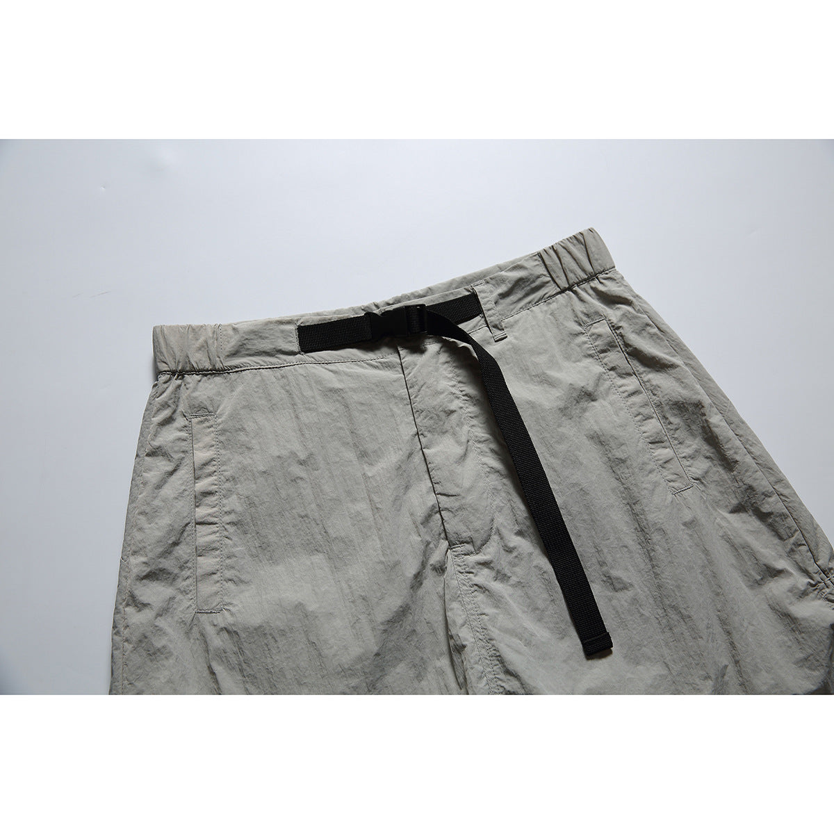 Close-up of gray pull-on bottoms with a black webbing belt, buckle, waistband, and front pockets.