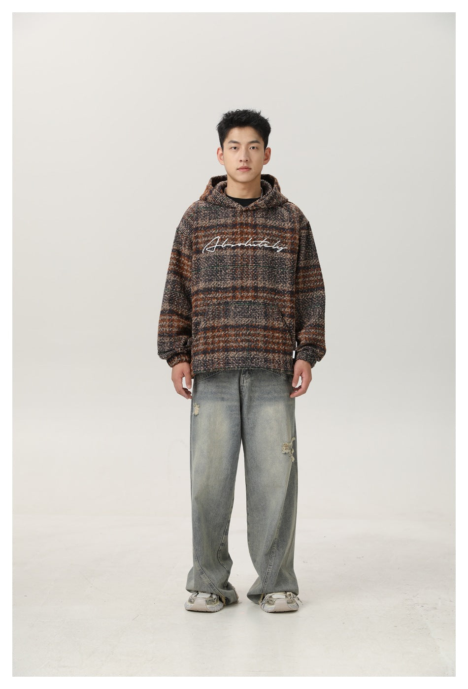 Man wearing plaid hooded top with white script embroidery and wide-leg faded jeans, front view