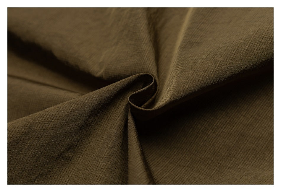 Close-up of olive-brown fabric gathered into folds, showing its fine grid-like texture.