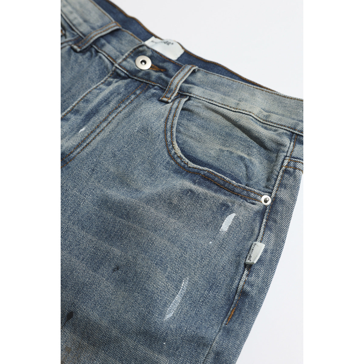 Close-up of faded blue jeans showing the front pocket, waistband button, belt loop and small distressed marks.