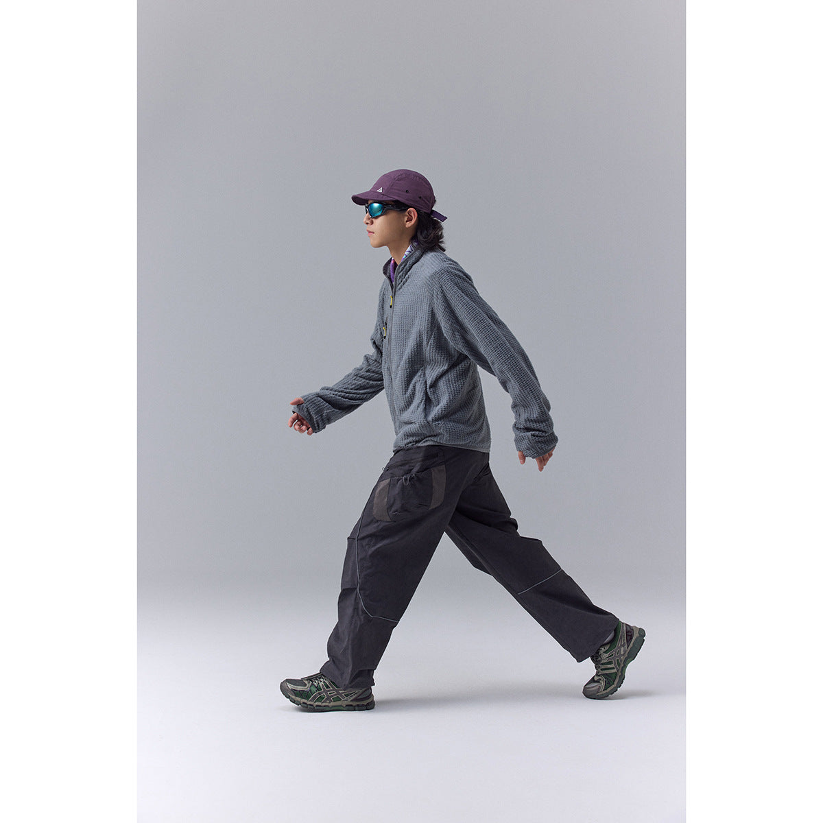Model walking in a slate-gray textured zip jacket, shown in side profile.